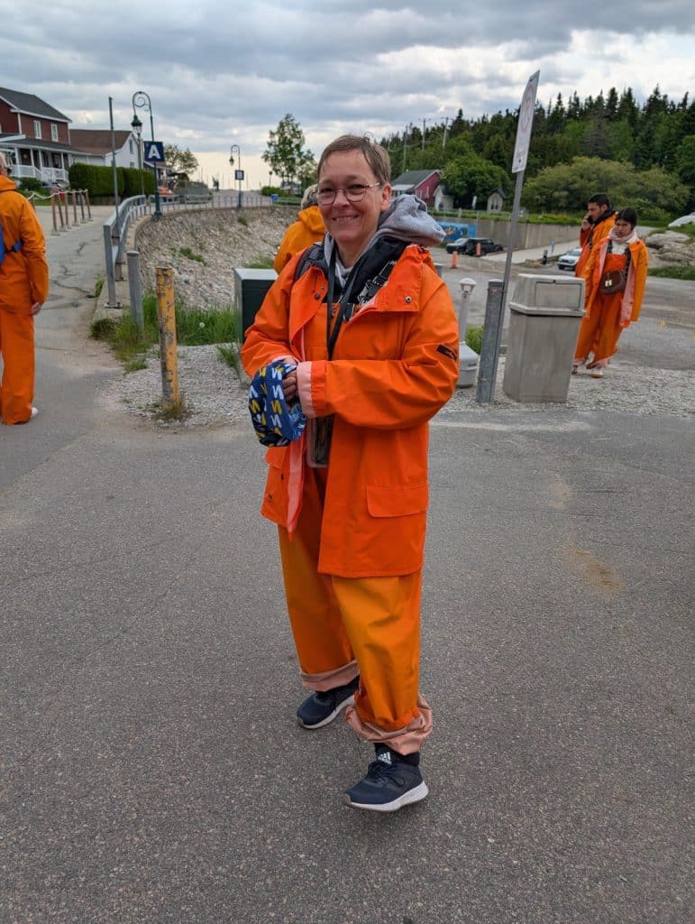 Susanne ist bereit für eine Waltour und trägt dabei einen leuchtend orangefarbenen Schutzanzug über ihrer Kleidung.