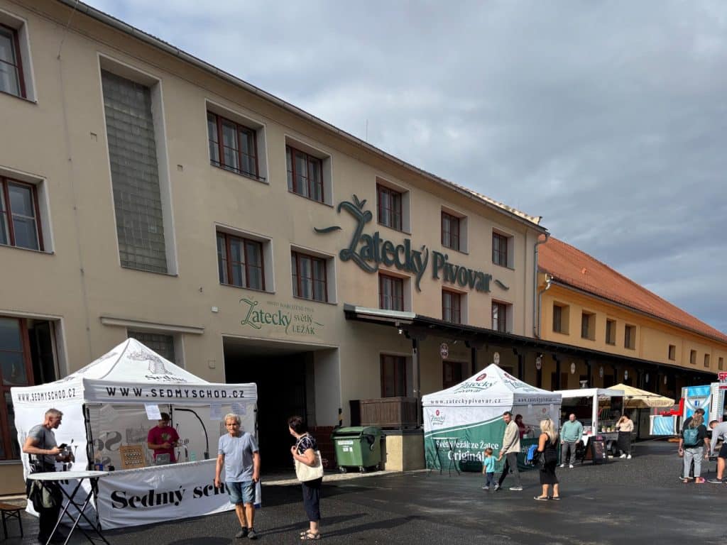 Auf dem Hopfenfest in Žatec stehen weiße Pavillons mit Werbeaufdrucken vor dem Gebäude der Brauerei Žatecký Pivovar, während Besucher über den Platz schlendern.