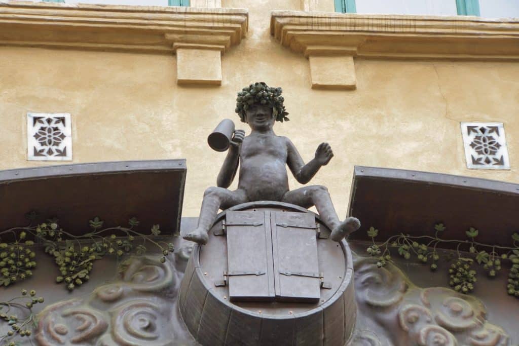 Eine Bronzestatue eines Mannes mit Hopfenkranz auf dem Kopf sitzt mit einem Bierkrug in der Hand auf einem Fass, das Teil der astronomischen Hopfenuhr in Žatec ist.