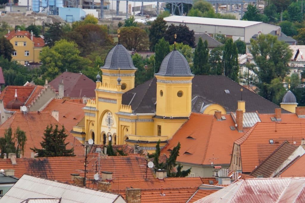 Blick über die Dächer von Žatec auf die markante gelbe Synagoge mit ihren zwei Türmen, die von grauen Kuppeln mit Davidsternen gekrönt sind.