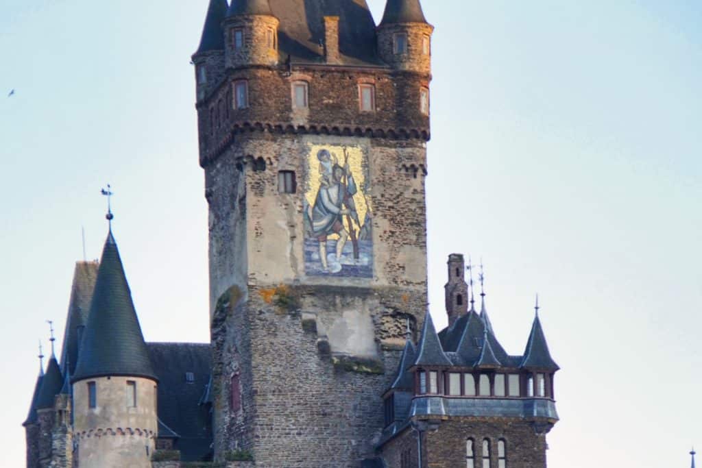 Ein großes, farbenfrohes Mosaik des Heiligen Christophorus ziert die Außenwand des massiven Hauptturms der Reichsburg Cochem, die von weiteren spitzen Türmen und Erkern umgeben ist.