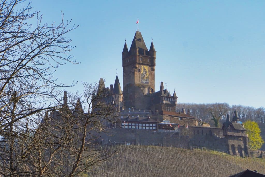 Die Reichsburg Cochem thront auf einem bewaldeten Hügel über Weinreben und präsentiert sich als imposante mittelalterliche Burganlage mit zahlreichen Türmen und Zinnen.