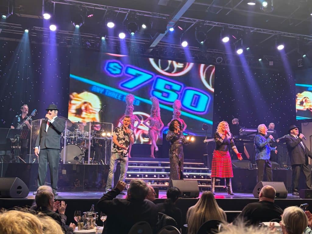 Eine Gruppe von Künstlern der Show „Berlin Stars in Concert“ tritt auf einer beleuchteten Bühne vor Publikum auf.