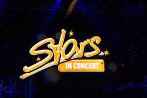Das Logo der Show „Stars in Concert“ in Berlin leuchtet in geschwungenen, gelben Neonbuchstaben vor einem dunklen Bühnenhintergrund mit kleinen Lichtpunkten.