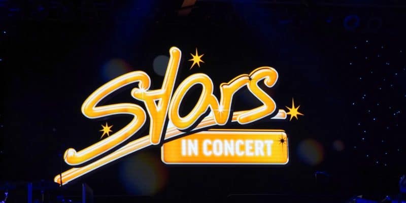 Das Logo der Show „Stars in Concert“ in Berlin leuchtet in geschwungenen, gelben Neonbuchstaben vor einem dunklen Bühnenhintergrund mit kleinen Lichtpunkten.