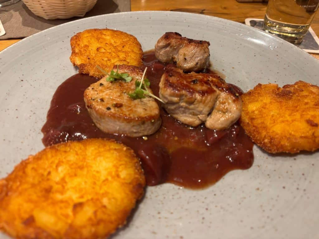Ein Hauptgang in einem Restaurant in Bremm, bestehend aus drei gebratenen Medaillons auf einer dunklen Sauce, serviert mit drei goldbraun gebackenen Kartoffelrösti auf einem hellen Teller.