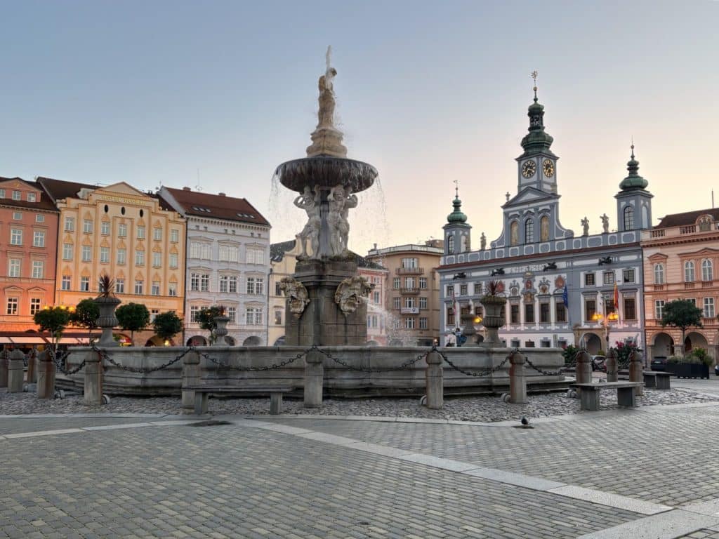 Der barocke Samson-Brunnen steht im Zentrum des Marktplatzes von Budweis, umgeben von historischen Gebäuden wie dem prachtvollen blauen Rathaus unter einem klaren Abendhimmel.