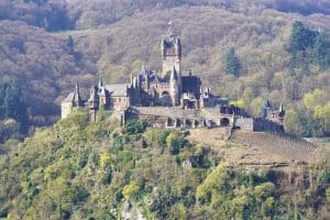 Die Reichsburg Cochem thront auf einem bewaldeten Hügel über Weinreben und präsentiert sich als imposante mittelalterliche Burganlage mit zahlreichen Türmen und Zinnen.