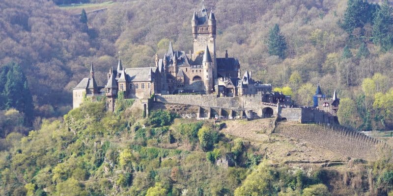Die Reichsburg Cochem thront auf einem bewaldeten Hügel über Weinreben und präsentiert sich als imposante mittelalterliche Burganlage mit zahlreichen Türmen und Zinnen.