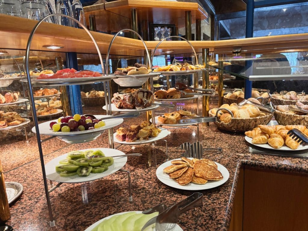 Ein reichhaltiges Frühstücksbuffet im Hotel Hegenbarth's bietet eine Auswahl an frischem Obst wie Kiwi und Weintrauben, verschiedenen Backwaren, Croissants, Brötchen und kleinen Pfannkuchen auf mehrstöckigen Etageren.