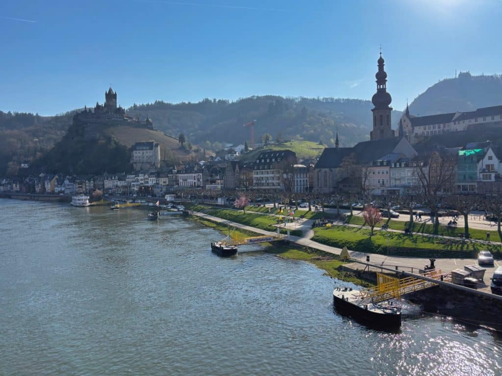 Blick auf die Stadt Cochem an der Mosel mit der Reichsburg auf einem Hügel im Hintergrund und der markanten St. Martin Kirche am Flussufer.