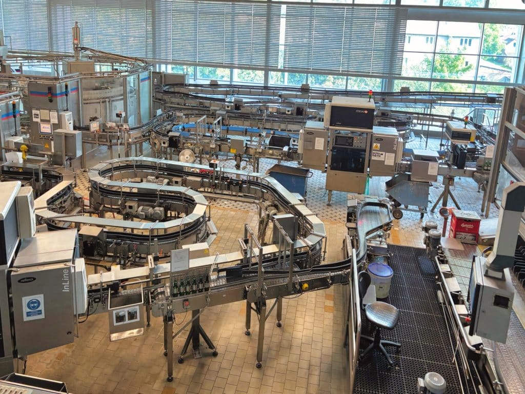 Blick von oben in die Abfüllhalle der Budweiser Brauerei mit komplexen Förderbandsystemen, Edelstahlanlagen und Flascheninspektionsmaschinen.