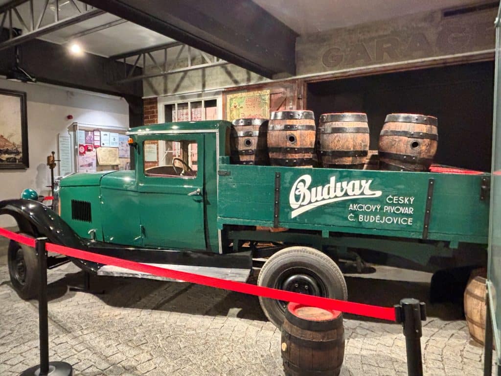 Ein grüner historischer Budvar-Lieferwagen mit Holzfässern auf der Ladefläche steht als Ausstellungsstück bei einer Brauereiführung in Budweis hinter einer Absperrung.