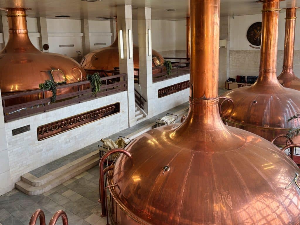 Große, glänzende Braukessel aus Kupfer stehen in einer hellen, gefliesten Halle der Brauerei in Budweis während einer Brauereiführung.