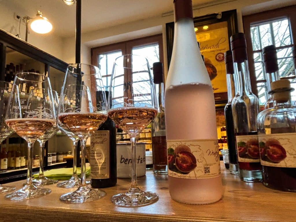 Drei mit roséfarbenem Secco gefüllte Weingläser stehen neben einer passenden, gekühlten Flasche auf einem Holztresen in einem gemütlichen Weingut in Cochem.