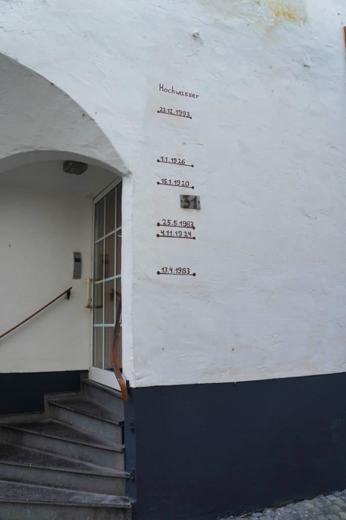 An einer weißen Hauswand in Cochem sind unter dem Wort „Hochwasser“ mehrere historische Hochwassermarken mit Daten wie 1993, 1926 und 1983 markiert, die den jeweiligen Wasserstand anzeigen.
