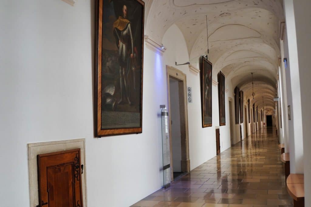 Der prunkvolle Kaisergang im Stift Melk zeigt einen langen, hellen Korridor mit gewölbter Decke, an dessen Wänden zahlreiche lebensgroße Porträts österreichischer Herrscher hängen.