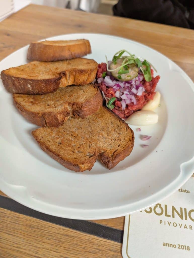 Ein Teller mit Rindertatar, garniert mit roten Zwiebeln und Kräutern, serviert mit gerösteten Brotscheiben und Knoblauchzehen im Restaurant Solnice in Budweis.