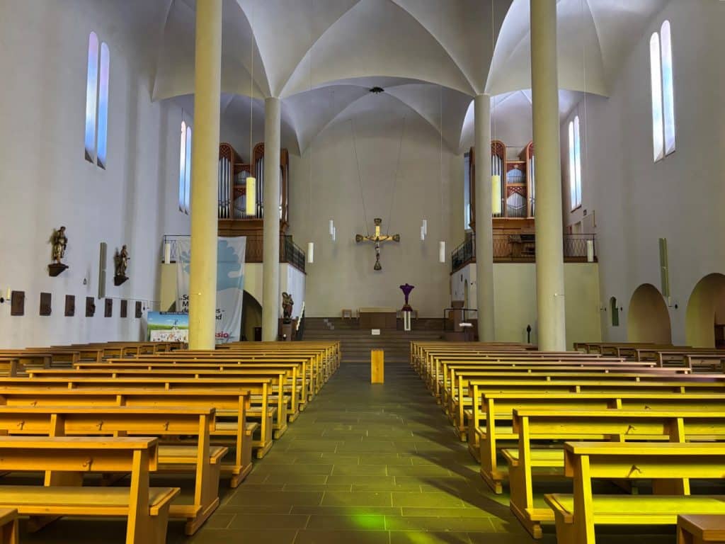 Innenansicht der katholischen Kirche St. Martin in Cochem mit hölzernen Kirchenbänken, hohen Säulen und einem großen Kruzifix über dem Altarraum.