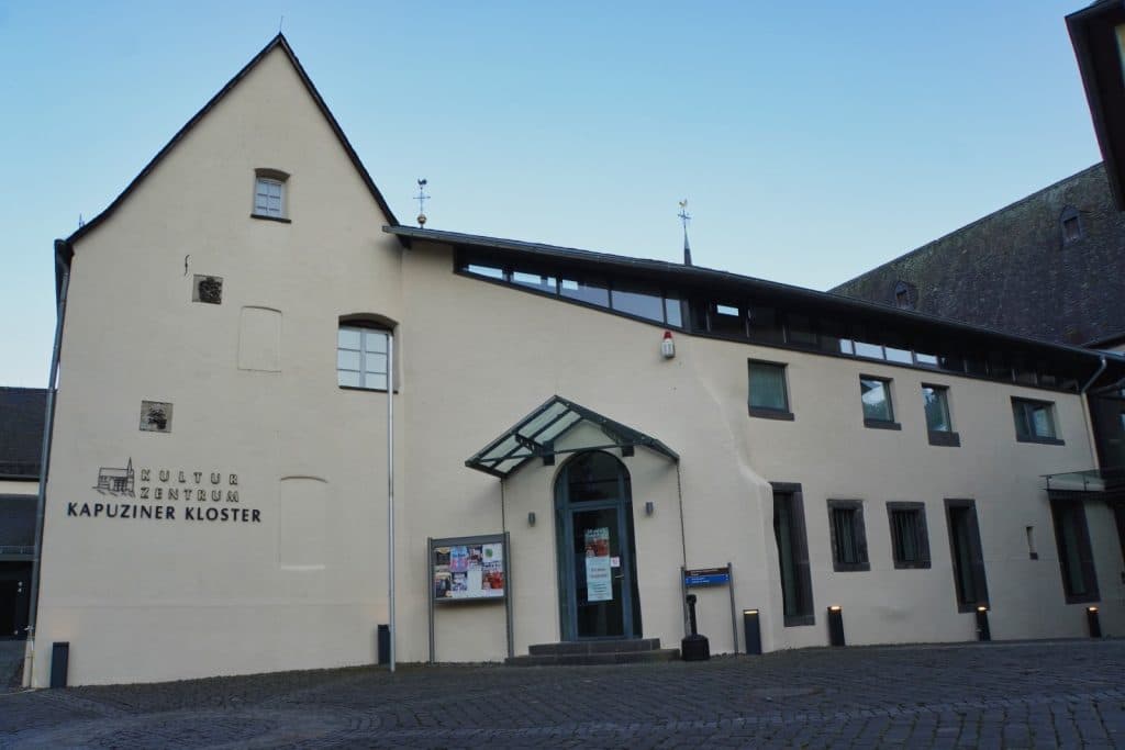 Das Kulturzentrum Kapuzinerkloster in Cochem präsentiert sich als helles, historisches Gebäude mit modernem Eingangsbereich und dem Schriftzug an der Fassade.