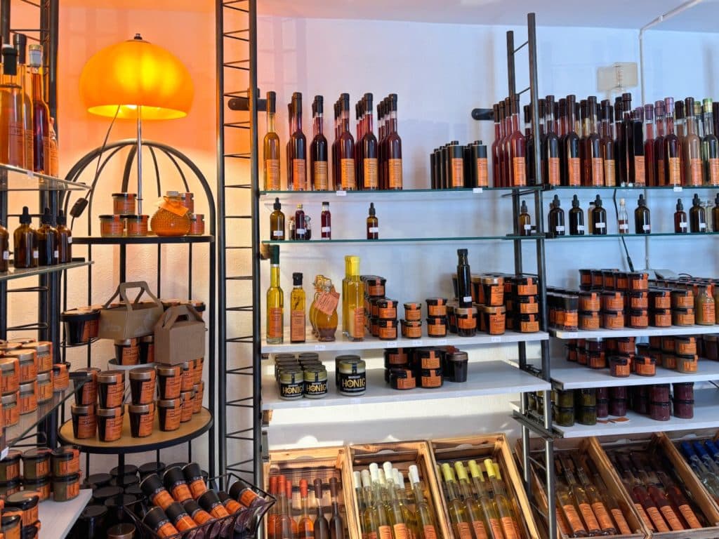 In einem Verkaufsraum der Essigkultur HB präsentieren sich zahlreiche Regale mit einer großen Auswahl an Essigflaschen, Honiggläsern und anderen Feinkostprodukten unter einer warm leuchtenden, orangefarbenen Lampe.
