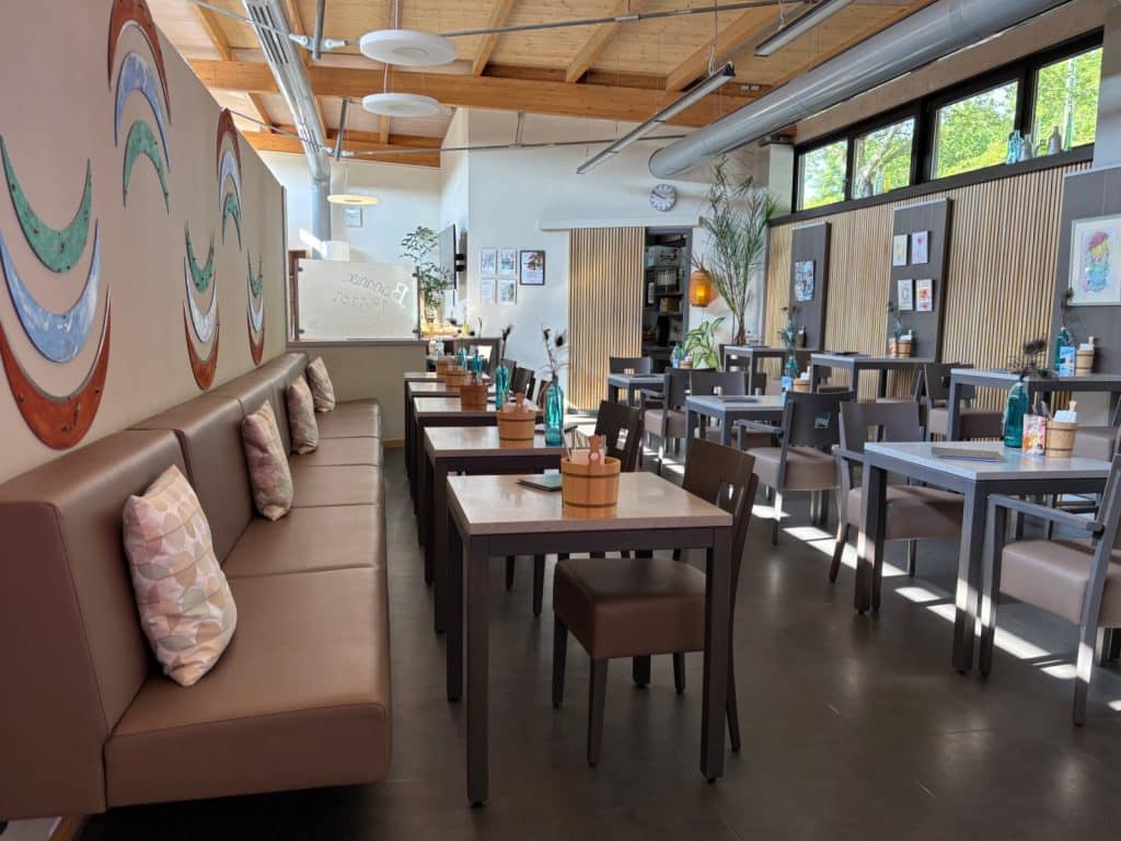 Ein modern gestalteter Gastraum im Restaurant der Therme Bad Sassendorf mit einer langen braunen Sitzbank, Holztischen und einer Wanddekoration aus bunten Sichelmonden.
