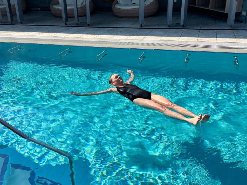 Eine Frau in einem schwarzen Badeanzug schwebt entspannt auf dem Rücken im Wasser eines Außenbeckens der Therme in Bad Sassendorf.