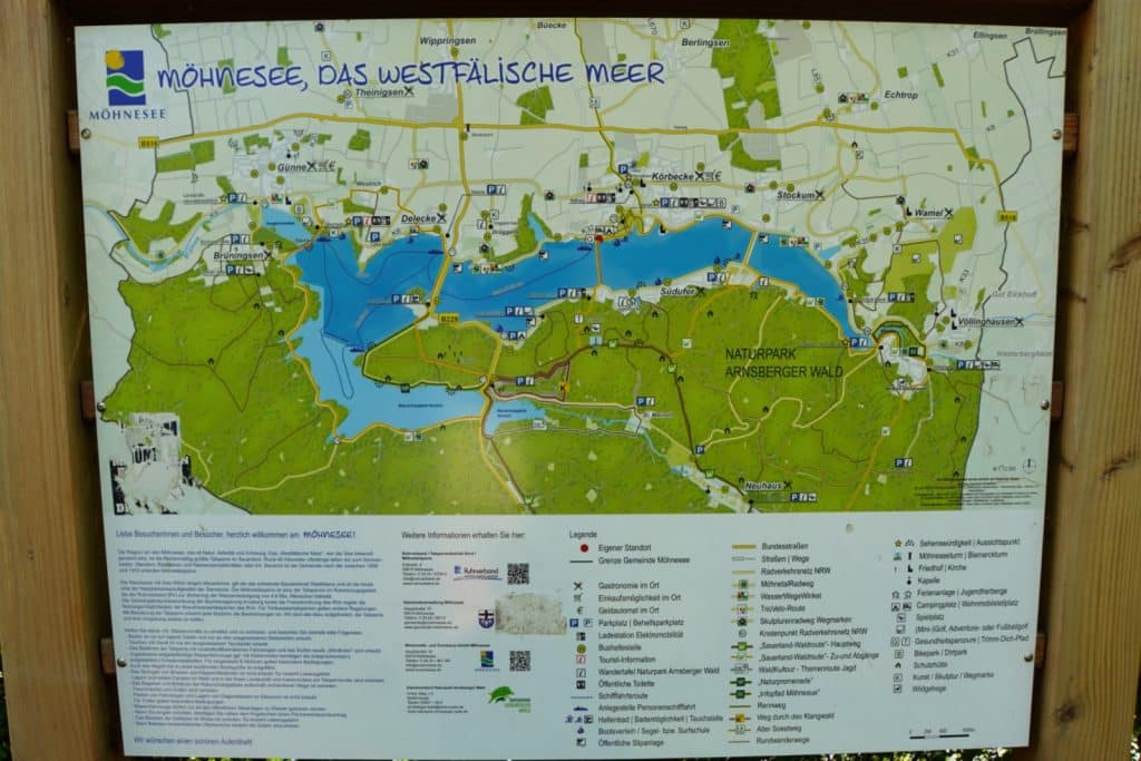 Eine detaillierte Übersichtskarte zeigt den Möhnesee, das "Westfälische Meer", eingebettet in den Naturpark Arnsberger Wald mit markierten Wanderwegen, Parkplätzen und Sehenswürdigkeiten. Unter der Karte befindet sich eine ausführliche Legende und Informationstexte für Besucher der Region.