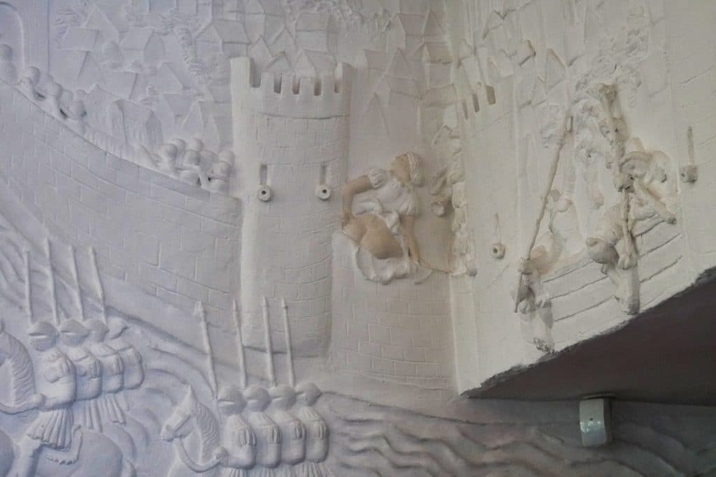 Ein weißes Wandrelief im Burghofmuseum in Soest zeigt eine mittelalterliche Belagerungsszene, bei der eine Frau auf der Stadtmauer ihr entblößtes Hinterteil den herannahenden Soldaten entgegenstreckt.