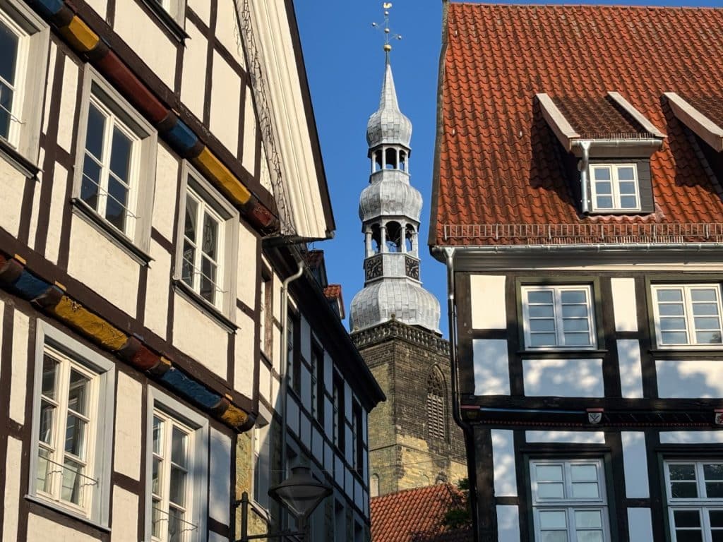 Blick durch eine schmale Gasse der Soester Altstadt auf den markanten Turmhelm der St. Petri-Kirche, eingerahmt von historischen Fachwerkhäusern mit weißen Fassaden und dunklen Holzbalken.