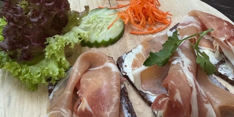 Vorspeise der Menüsafari in Soest im Brauhaus Zwiebel: Pumpernickel mit weißem Aufstrich und Schinken, garniert mit Salat, Gurke und geraspelten Karotten auf einem Holzbrett.