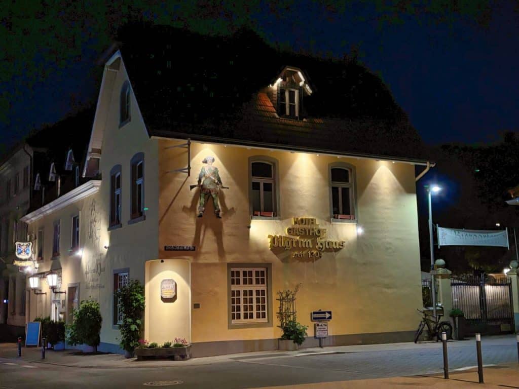 Das beleuchtete Hotel Gasthof Pilgrim Haus in Soest bei Nacht, ein historisches gelbes Gebäude mit einer markanten Pilgerfigur an der Fassade.