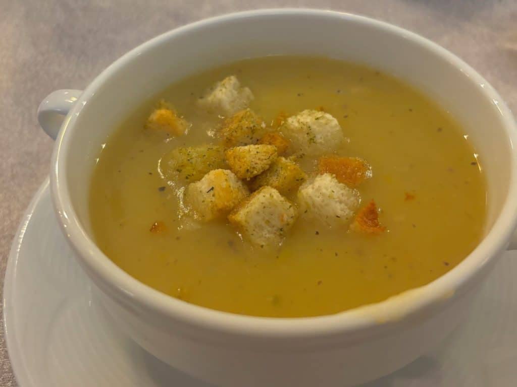 Eine weiße Tasse mit einer sämigen Kartoffelsuppe aus dem Ratskeller in Soest, die mit goldbraun gerösteten Croutons und Kräutern garniert ist.