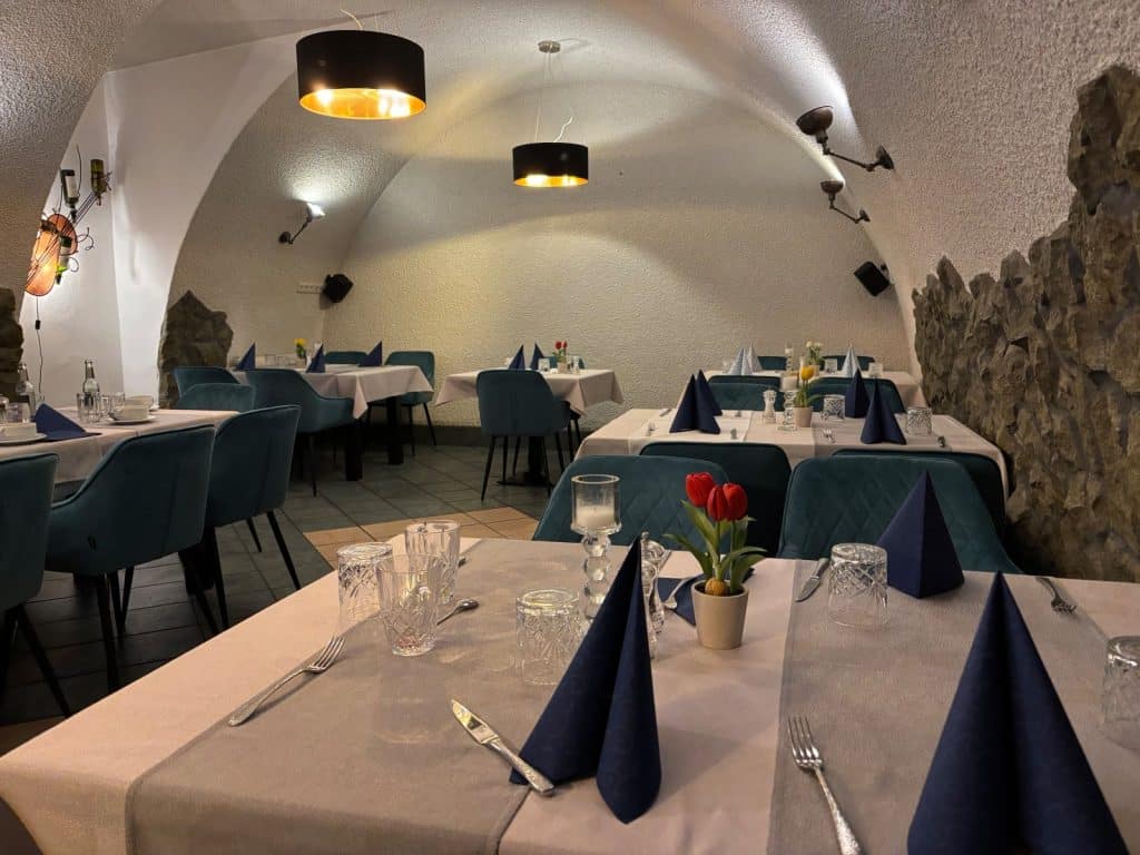 Menüsafari in Soest: Der gemütliche Gastraum des Ratskellers in Soest ist mit weiß eingedeckten Tischen, blauen Samtstühlen und blauen Stoffservietten unter einem gewölbten Deckengewölbe eingerichtet.