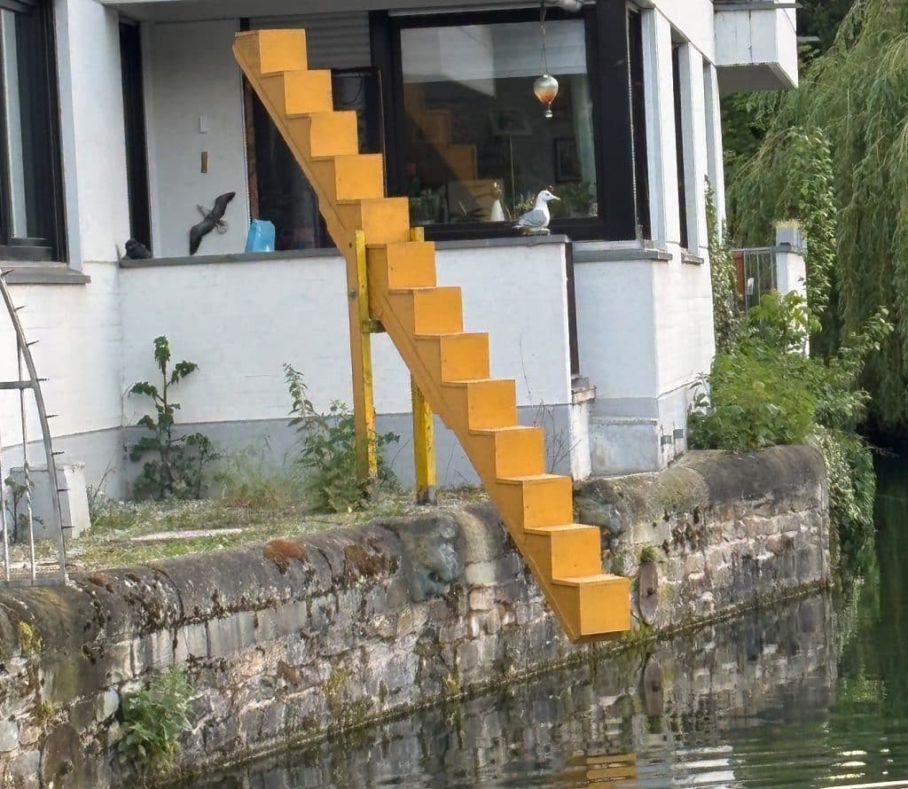 Die Soester Wippe ragt von einer Ufermauer über das Wasser eines Kanals vor einem weißen Gebäude.
