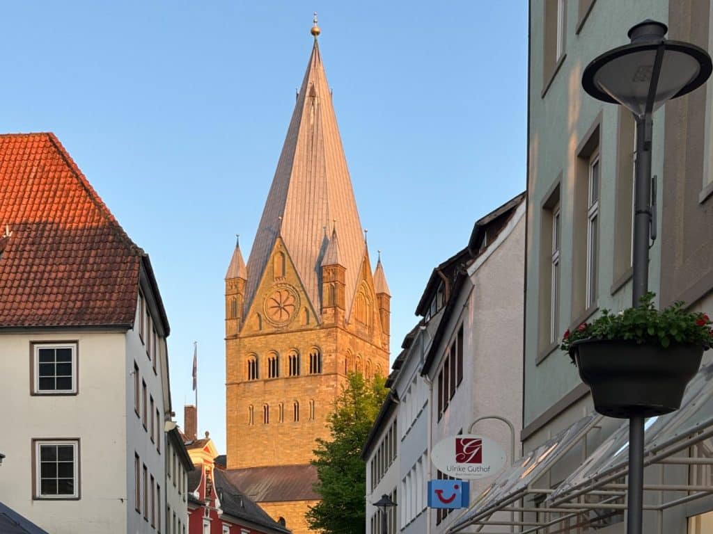 Blick durch eine schmale Gasse auf den massiven Turm des St.-Patrokli-Doms in Soest, dessen romanische Architektur im warmen Abendlicht erstrahlt.
