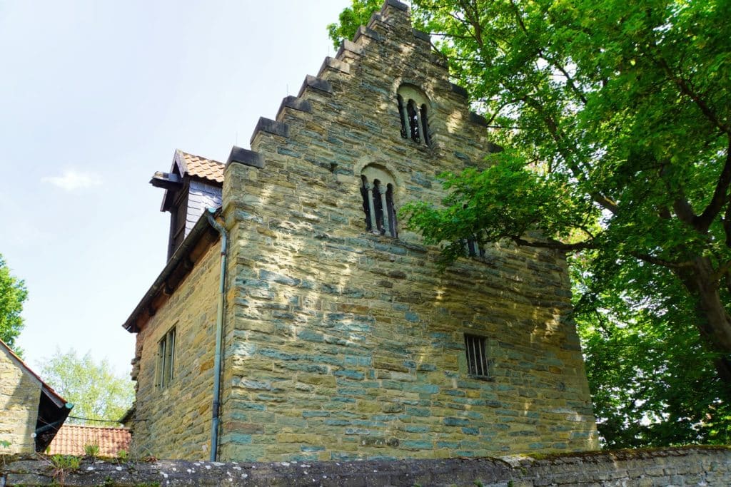 Das romanische Haus in Soest präsentiert sich als massives Steinbauwerk mit einem markanten Treppengiebel und schmalen, gekoppelten Rundbogenfenstern unter einem hellen Himmel.