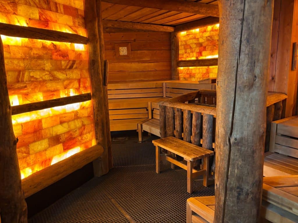 Innenansicht einer Sauna in der Börde Therme Bad Sassendorf mit Holzbänken, rustikalen Baumstämmen und hinterleuchteten Wänden aus orangefarbenen Salzsteinen.