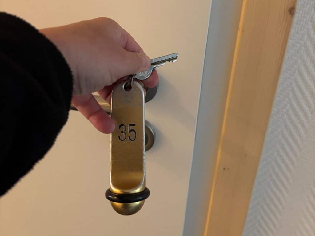 Eine Hand hält einen metallischen Zimmerschlüssel des Hotel Haus Griese am Möhnesee mit der eingravierten Nummer 35 vor eine weiße Zimmertür.