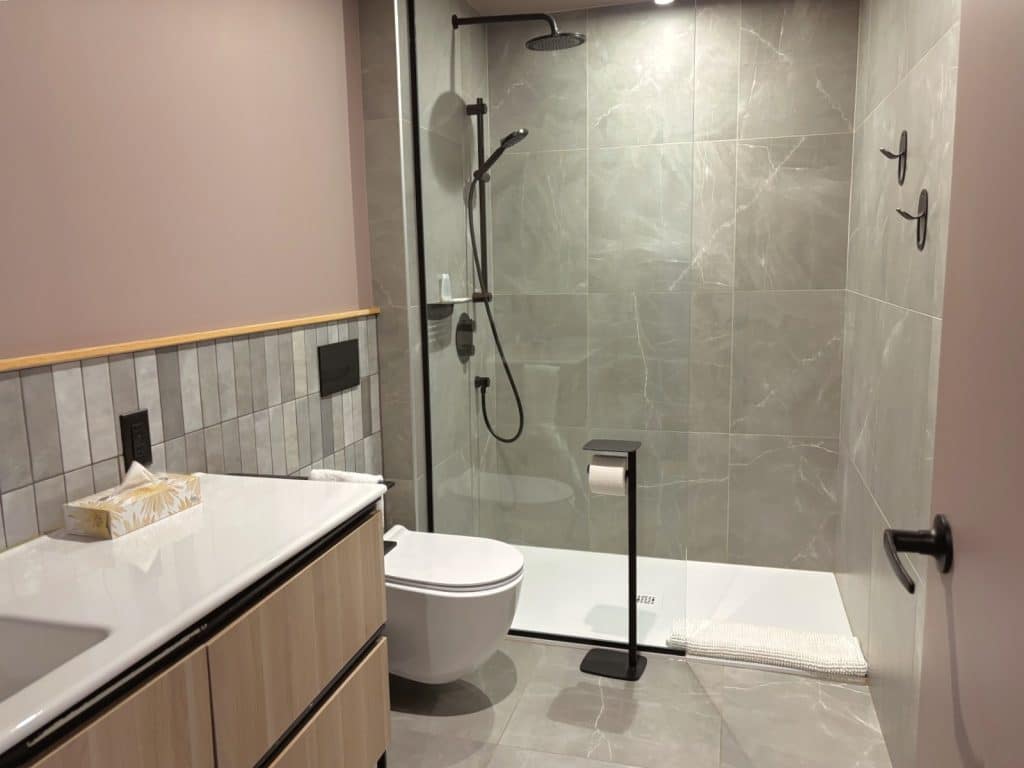 Modernes Badezimmer in Les Lofts Dorchester in Québec mit einer begehbaren Glasdusche, grauen Marmorfliesen, einer wandhängenden Toilette und einem hellen Holzwaschtisch mit weißer Platte.