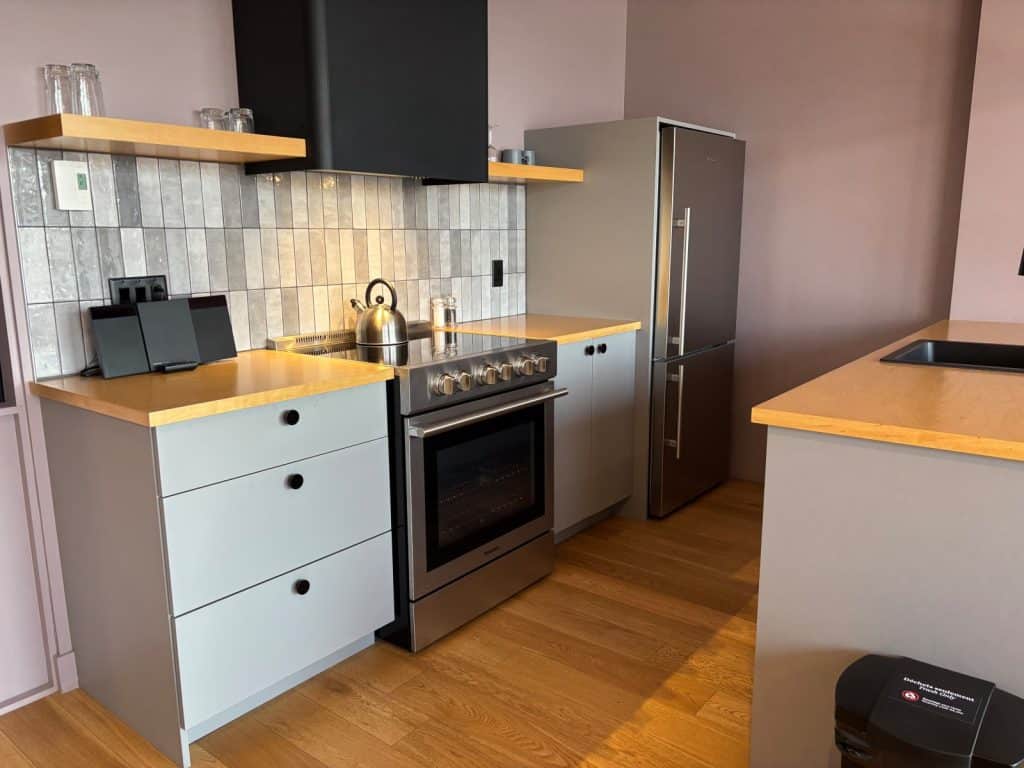Moderne Küche in Les Lofts Dorchester in Québec mit hellgrauen Schränken, Holzoberflächen, einem Edelstahlherd und einem passenden Kühlschrank vor einer lila Wand.