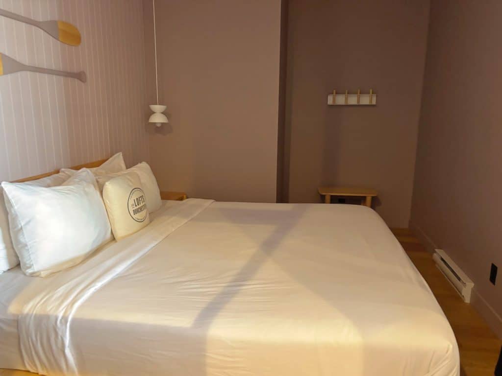Ein Schlafzimmer in einer Wohnung in Québec mit einem großen Bett mit weißer Bettwäsche, dekorativen Rudern an der Wand und einer minimalistischen Einrichtung in sanften Erdtönen.