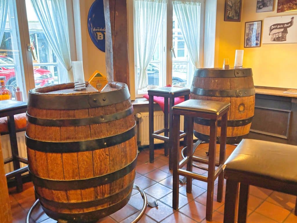 Brauhaus in Soest: Rustikaler Innenraum der Brauerei in Soest mit zwei großen Holzfässern, die als Tische dienen, umgeben von hohen Barhockern vor hellen Fenstern.