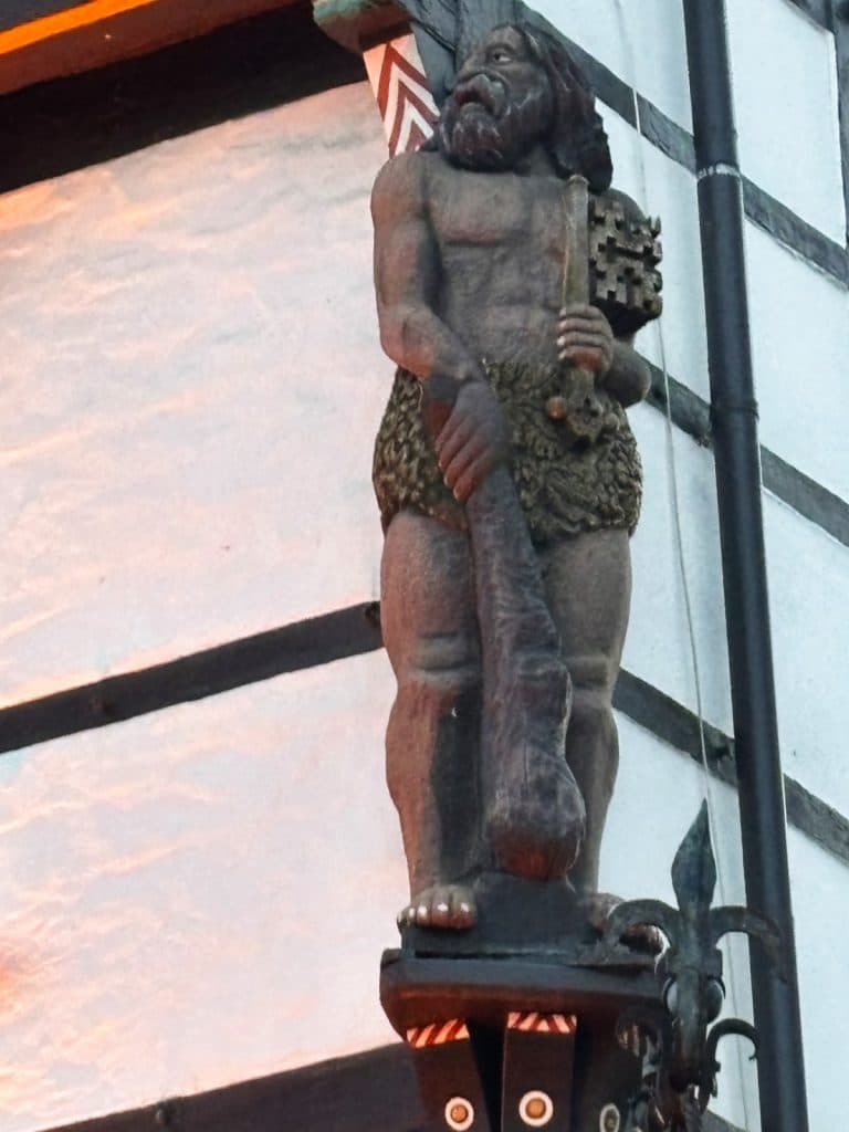 Eine hölzerne Skulptur eines „Wilden Mannes“ mit Bart, Keule und Schlüssel an der Fassade eines historischen Fachwerkhauses in Soest.