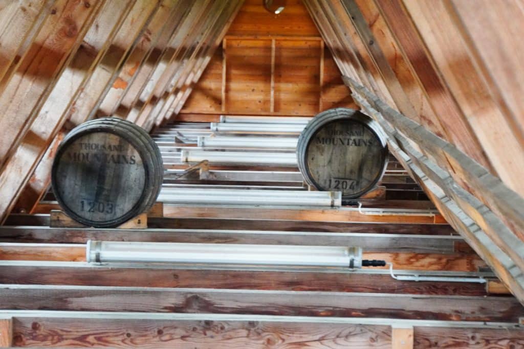 Zwei Holzfässer mit der Aufschrift „Thousand Mountains“ lagern auf Holzbalken unter dem spitzen Dach des Gradierwerks Bad Sassendorf
