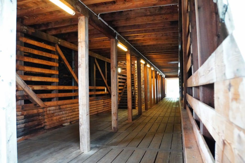 Innenansicht eines hölzernen Gangs im Gradierwerk Bad Sassendorf mit beleuchteten Stützpfeilern, Holzdielenboden und seitlichen Reisigwänden.