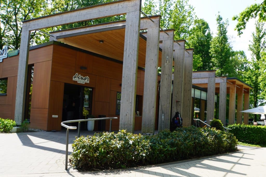 Das moderne Lino's Eis & Café im Kurpark von Bad Sassendorf präsentiert sich mit einer markanten Holzfassade und einer architektonisch auffälligen Pergola-Konstruktion aus hellen Holzbalken.