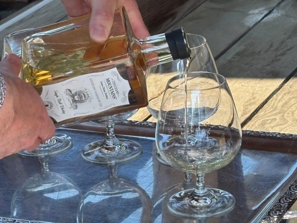 Eine Person schenkt bei einem Tasting im Kurpark von Bad Sassendorf „Thousand Mountains“ Single Malt Whisky aus einer eckigen Flasche in bauchige Gläser ein.