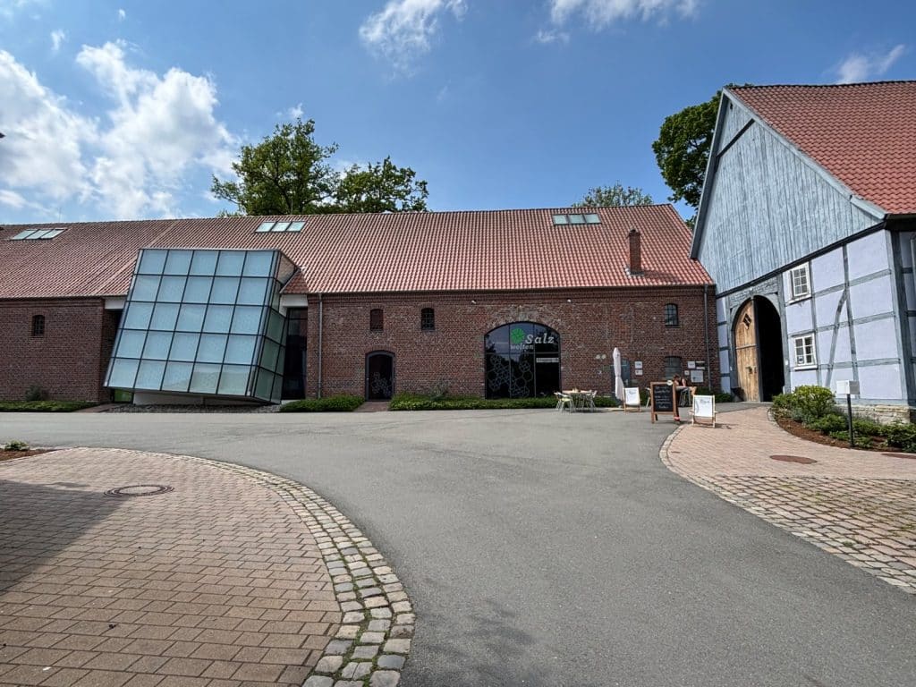 Das Erlebnismuseum Westfälische Salzwelten in Bad Sassendorf zeigt sich in einem historischen Backsteingebäude mit einem modernen, schräg angesetzten Glasvorbau und einem gepflasterten Vorplatz unter blauem Himmel.