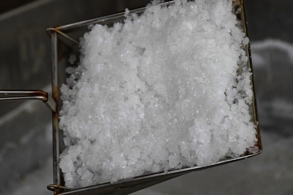 Ein quadratisches Metallsieb ist bis zum Rand mit frisch geschöpftem, grobkörnigem weißem Salz aus den Salzwelten Bad Sassendorf gefüllt.